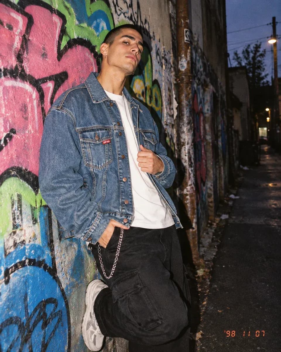 Man in a stonewashed denim jacket against a graffiti wall in flash light