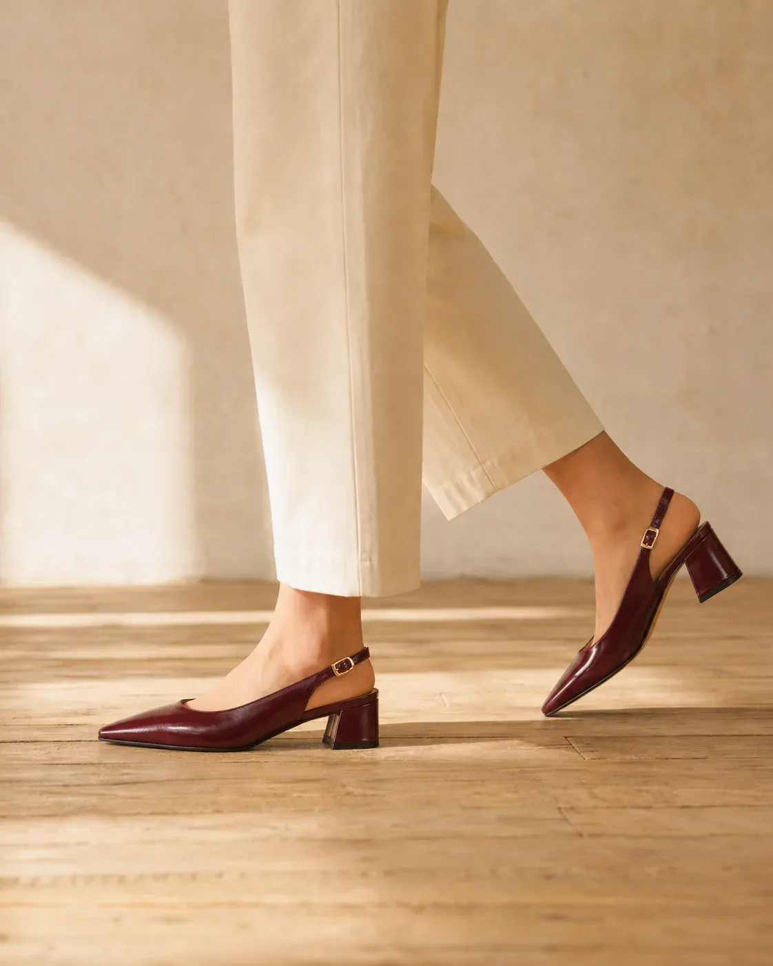 Oxblood slingback heels worn by a model walking on a wood floor